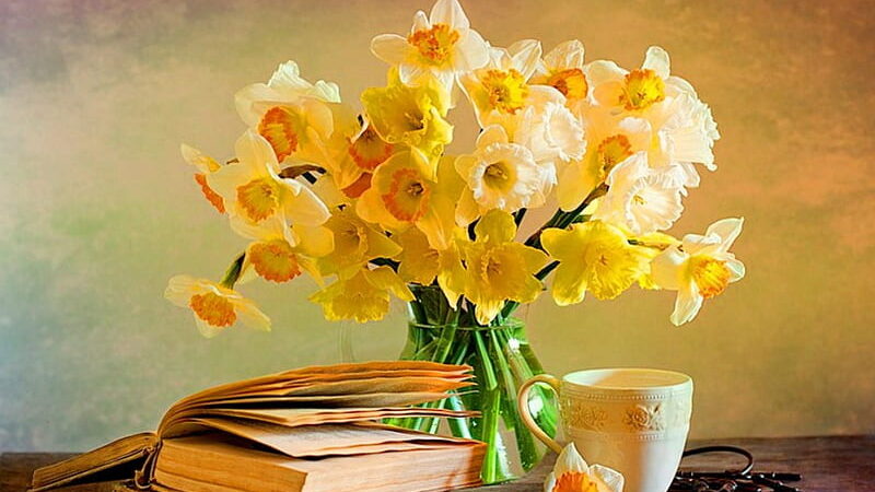 Image of a pile of books next to a vase of daffodils and a cup of tea