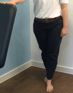 standing with one foot in front of the other, one hand on chair for support