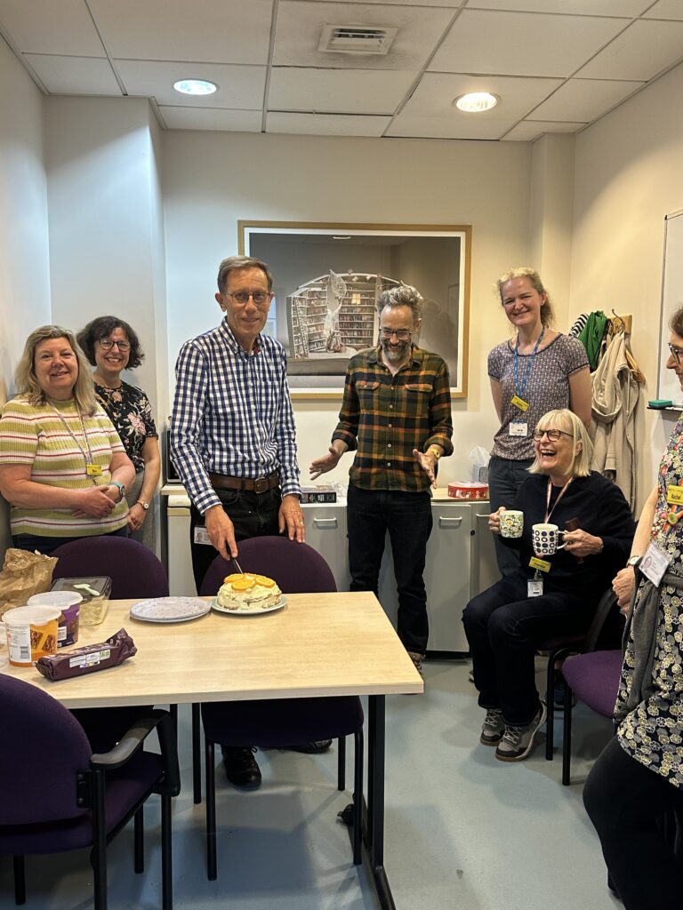 Library staff saying goodbye to Roland who is cutting the cake