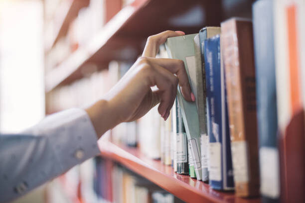 Photograph of someone's arm searching through books on a library shelf
