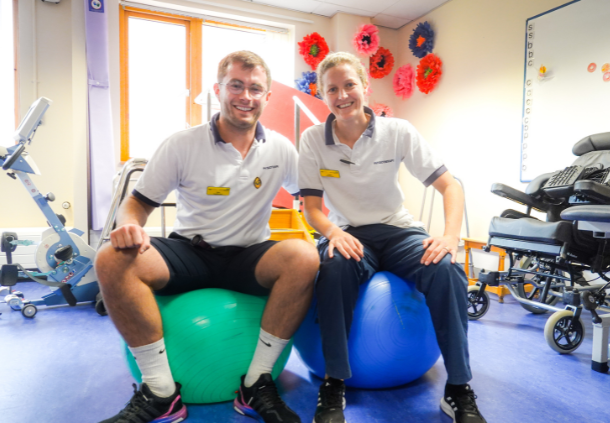 Two physiotherapists sat on therapy balls in a rehab space